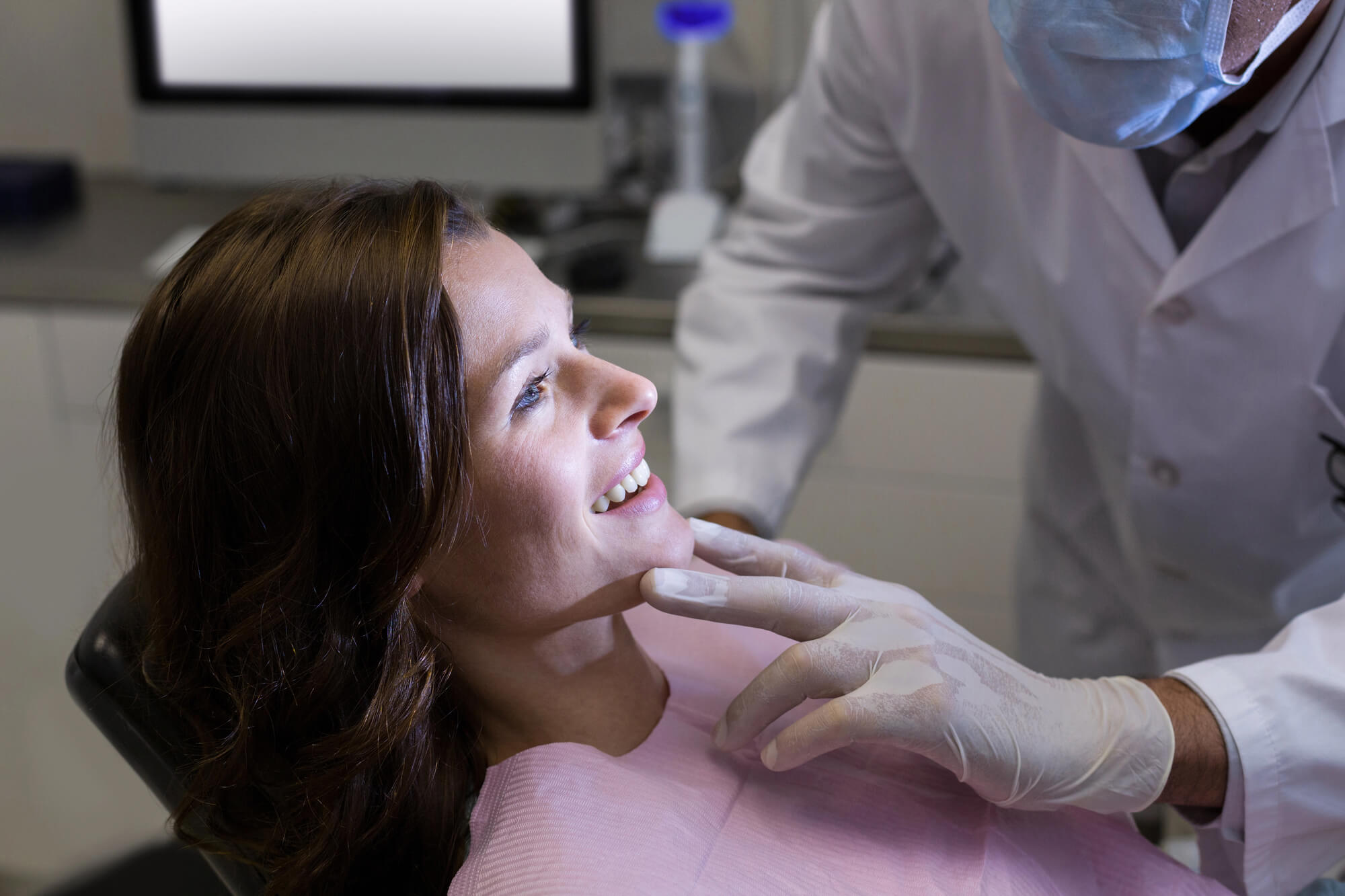 Orthodontist wearing white gloves and labcoat checks on female patient during visit