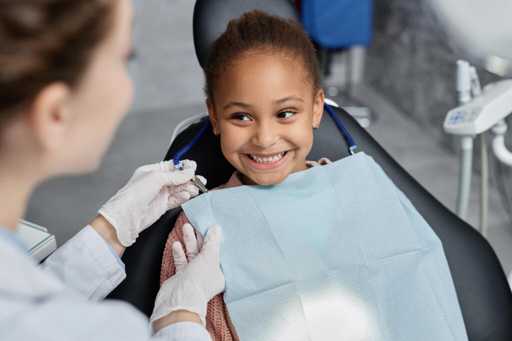 Young girl smiles to orthodontic provider during office visit while seated in chair