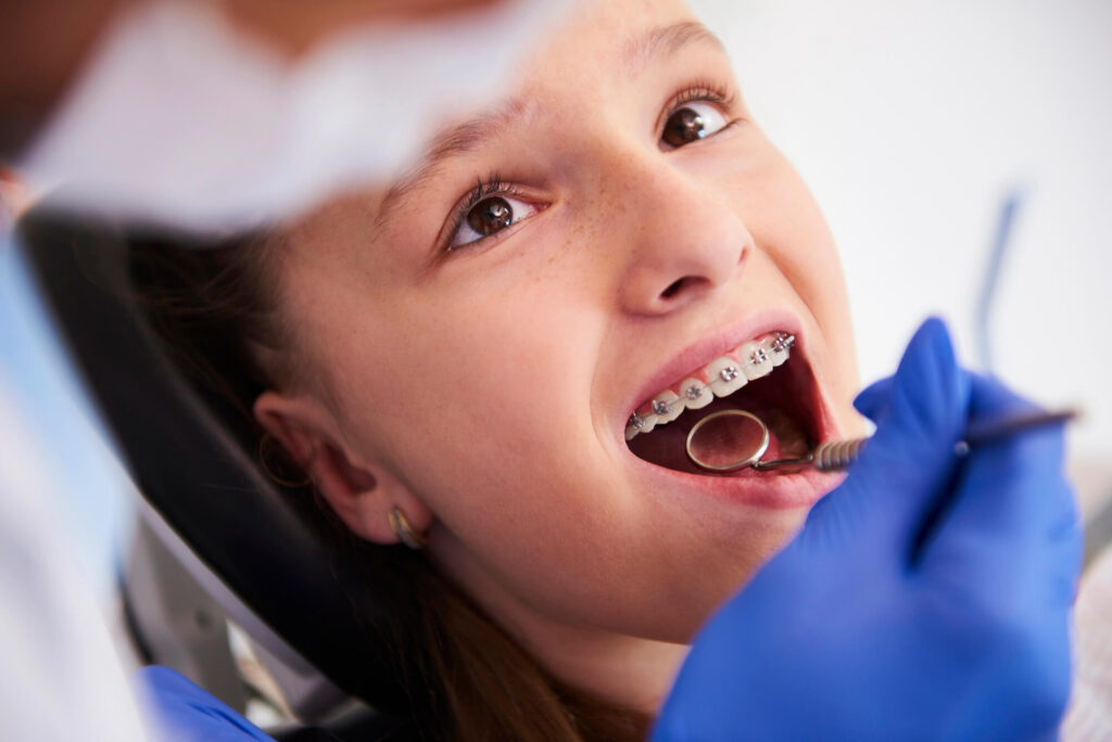 Orthodontist exams young female braces patient during office checkup