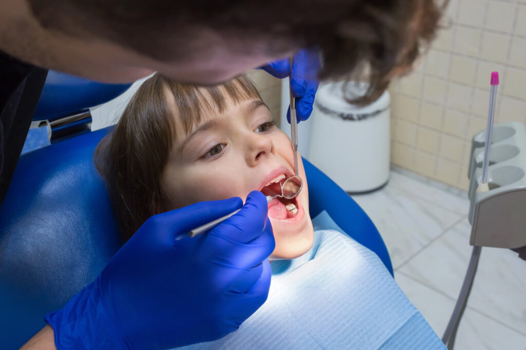 Orthodontist wearing blue gloves checks teeth of child patient during checkup