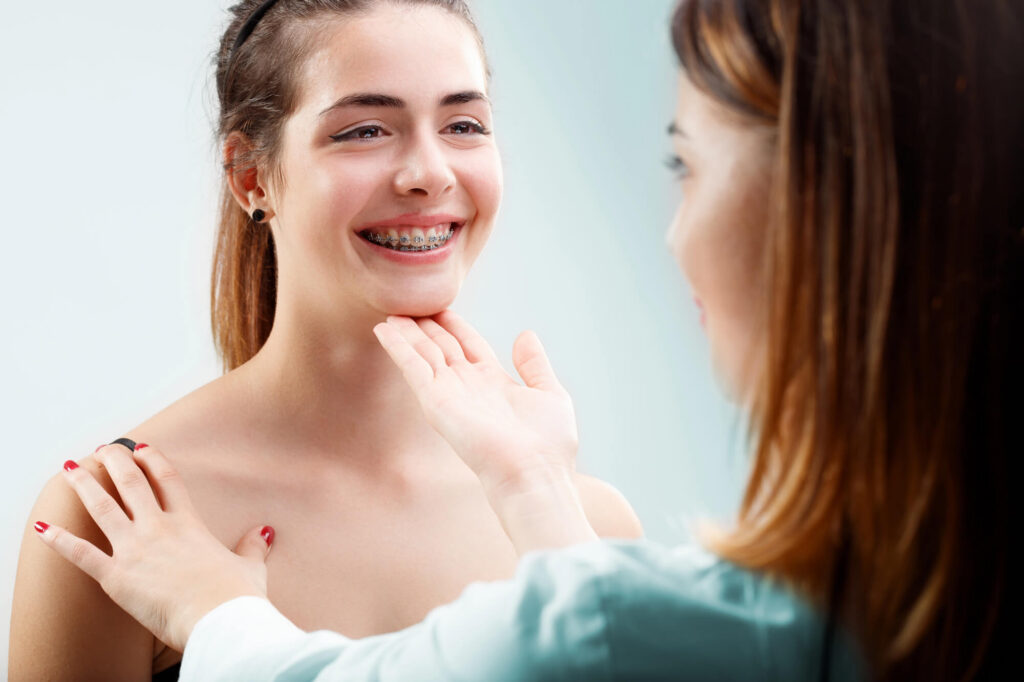Female teen braces patient smiles while orthodontic provider holds her chin up