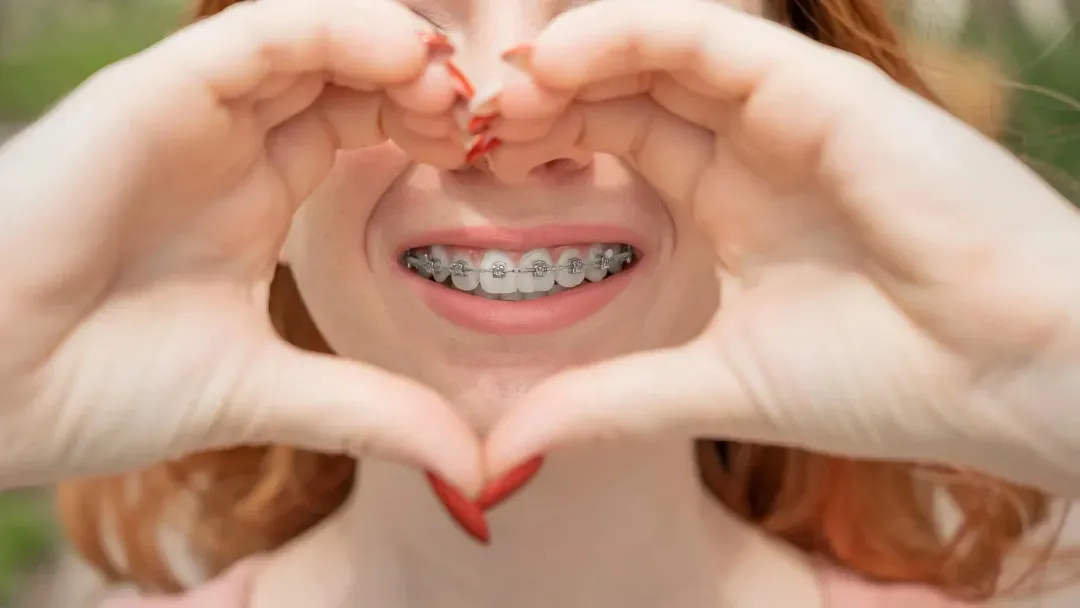 Woman with metal braces makes heart with her hands and smiles