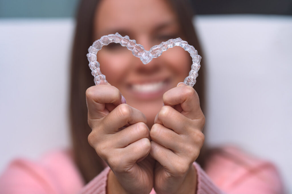Woman with perfect smile holding retainers in a heart shape.