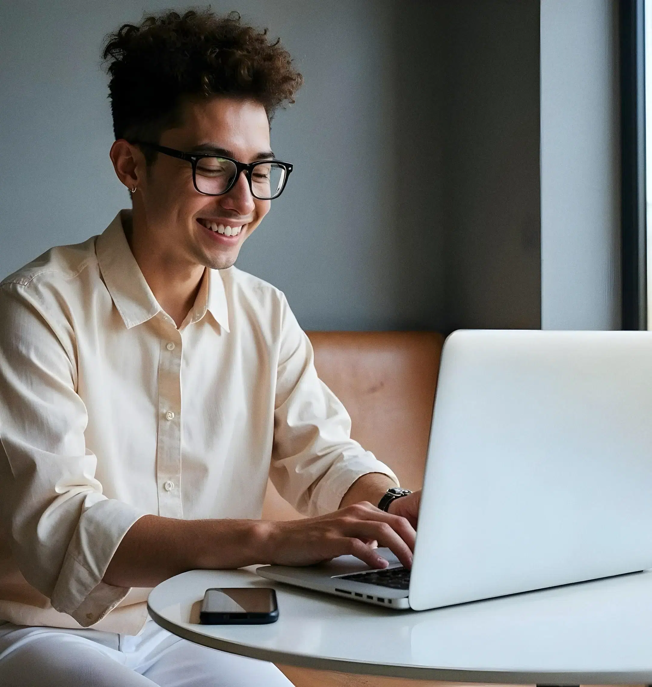 Young Man Smiling While Using Laptop Bright Cafe Setting